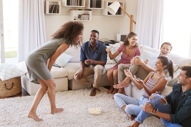 A group of people enthusiastically playing charades, smiling, and laughing indoors 