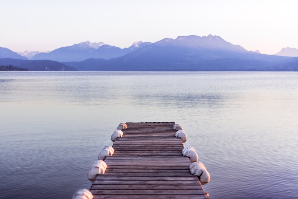 A dock leading into the flat water of a lake with hazy mountains in the background