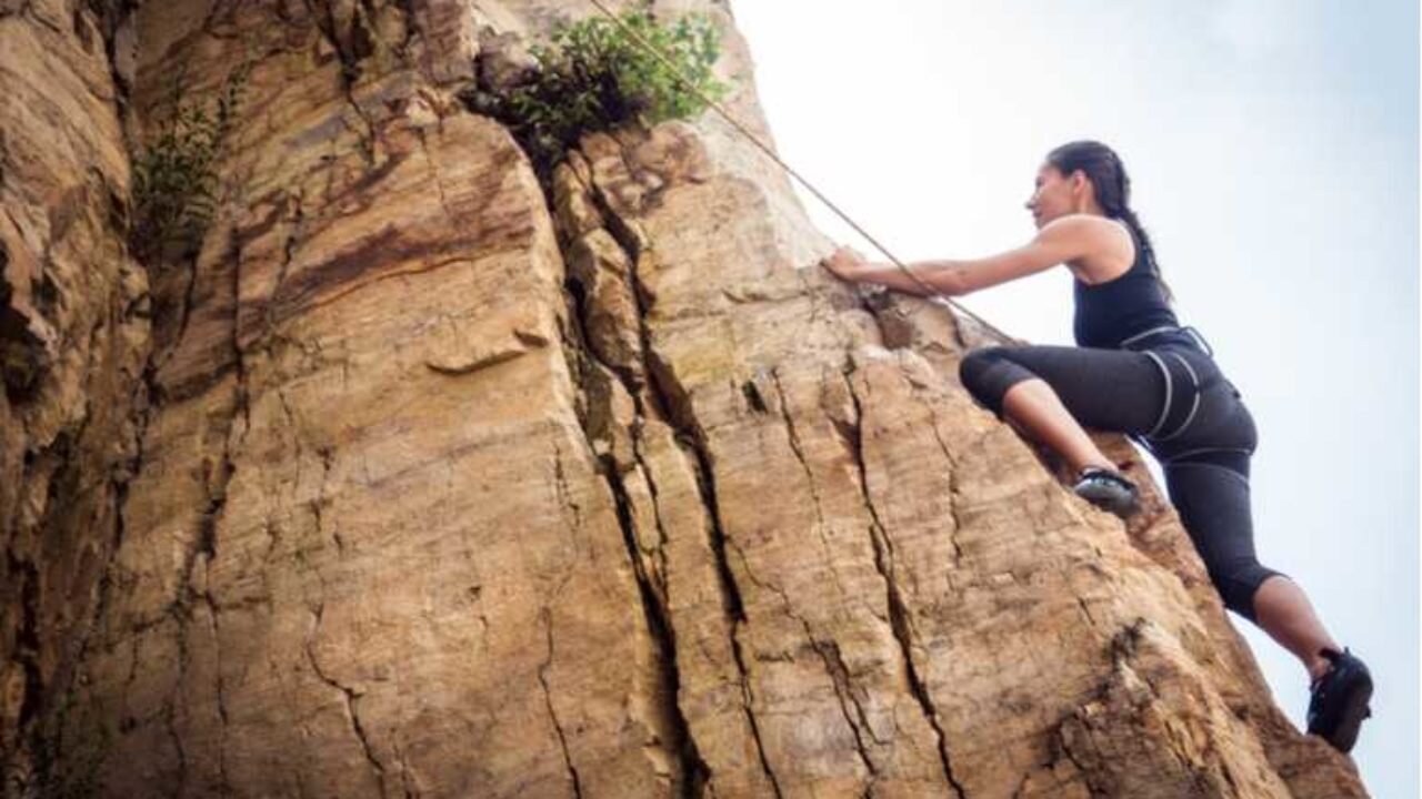 Someone in athletic wear and rock-climbing gear climbing a rock outdoors