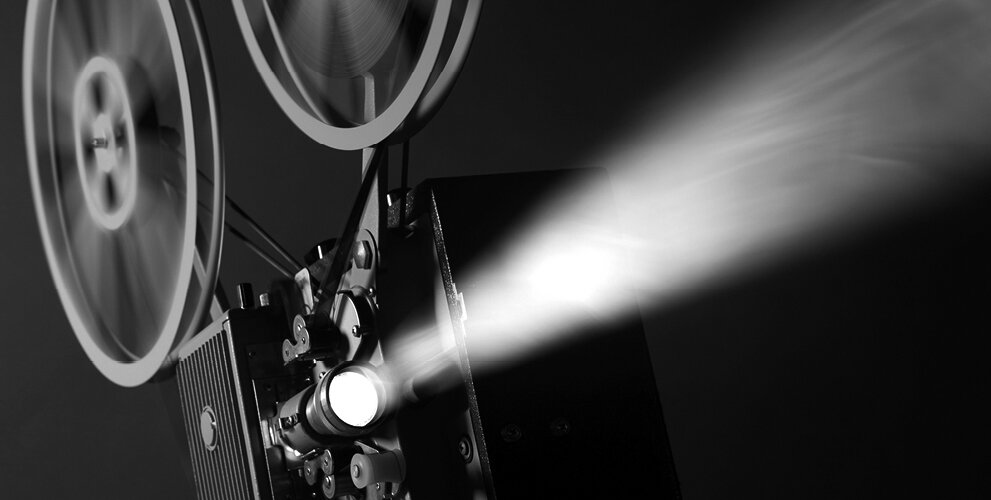 A black and white photograph of a film projector projecting light 