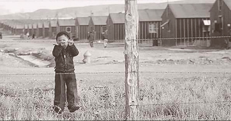 A sepia image from the film 'The Film Our Lost Years' featuring a child behind a barbed wire fence with an encampment in the backgrounds