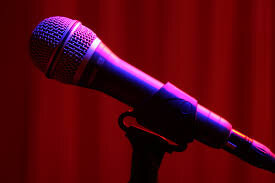 A microphone illuminated by a pink light with red curtains in the background