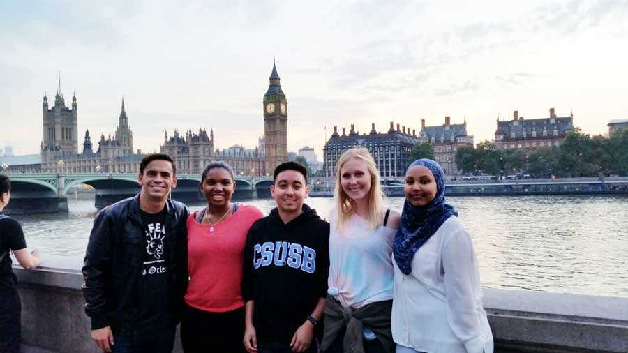 Five students smiling and posing in front of a European skyline featuring ornate buildings and a body of water 