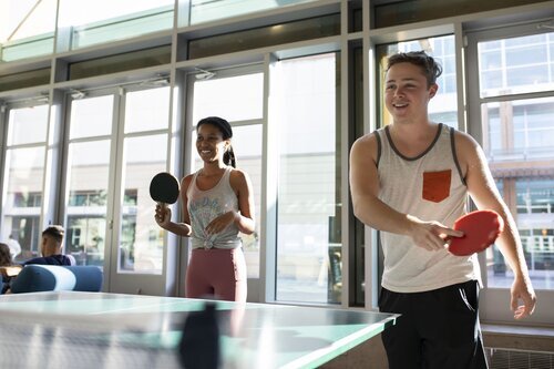 Two people smiling while playing table tennis in the Campus Recreation Center