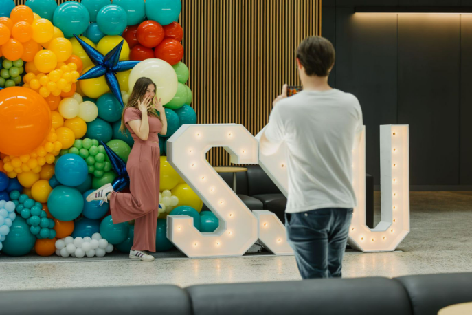 Someone posing with a lighted 'SSU' sign and colorful balloon display