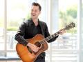 Andy Grammer smiling while playing an acoustic guitar 
