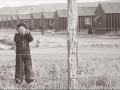 A sepia image from the film 'The Film Our Lost Years' featuring a child behind a barbed wire fence with an encampment in the backgrounds