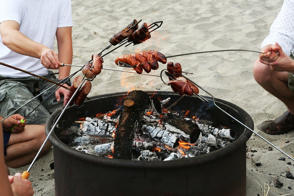 A group of people barbecuing hot dogs over a fire pit