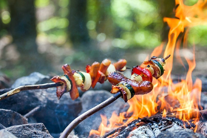 Skewers of vegetables being roasted over a campfire 