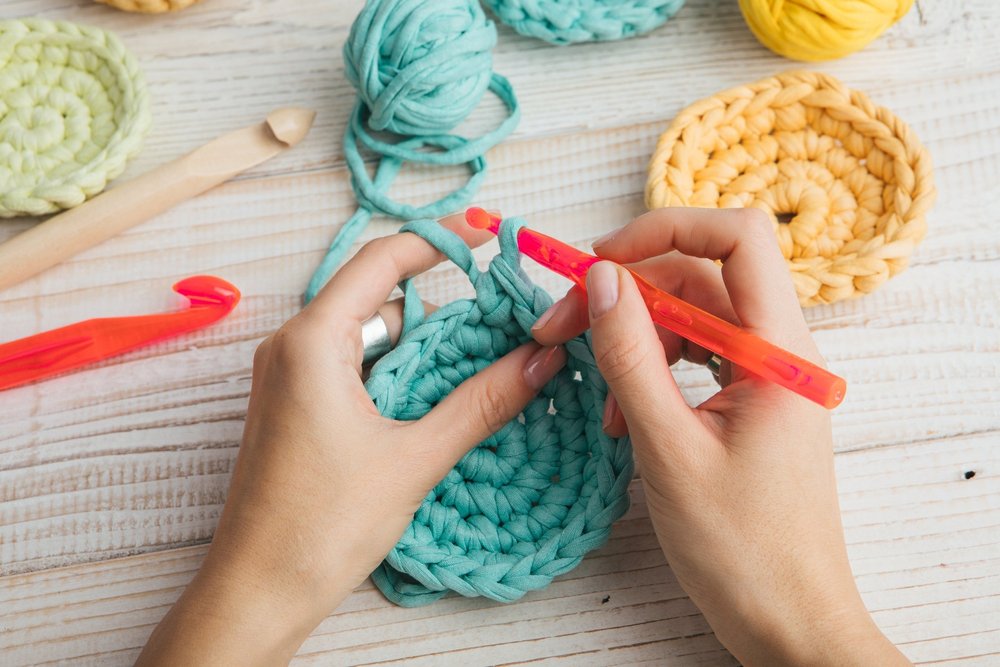 Hands crocheting with teal yarn and red crochet hooks