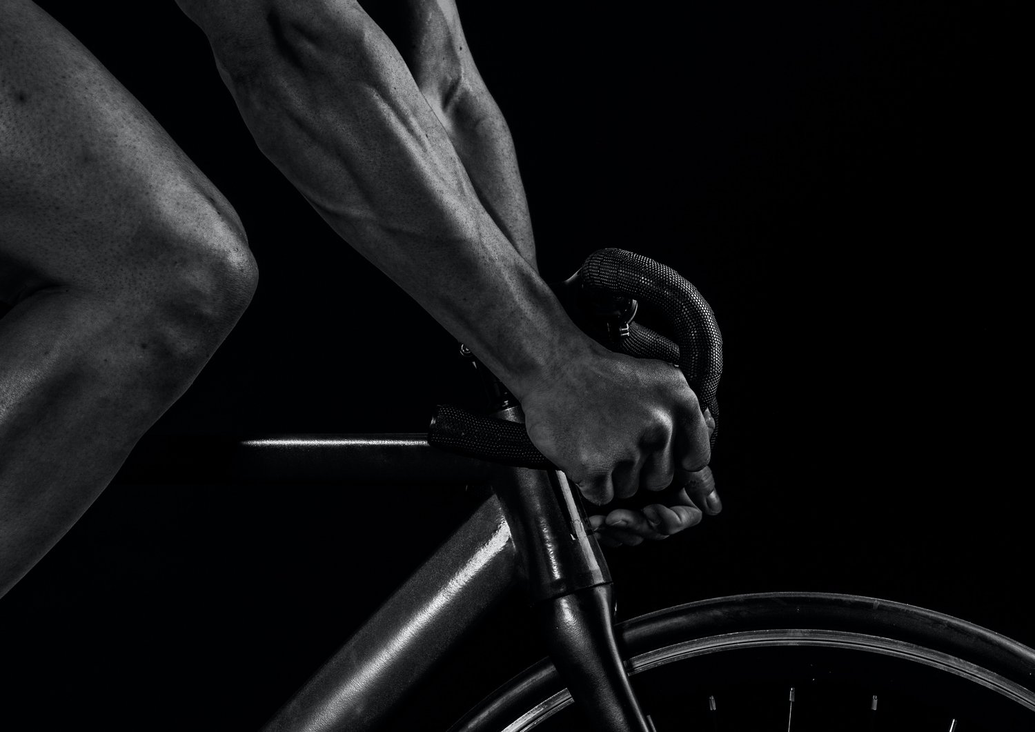 close up of hands on steering wheel on bicycle with knee in view in black and white