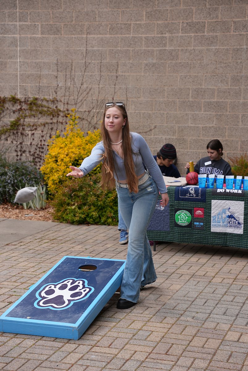 A student playing corn hole in front of the Campus Recreation building 