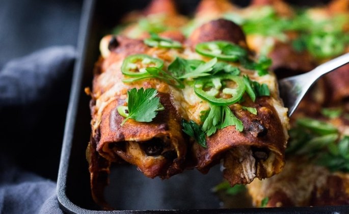 A fork lifting enchiladas from a pan