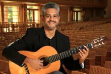Portrait of Eric Cabalo smiling and posing with their guitar inside an auditorium 