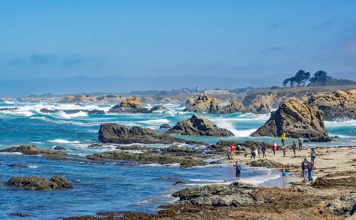 Ocean waves, rock formations, and people walking the shore at Fort Bragg Beach