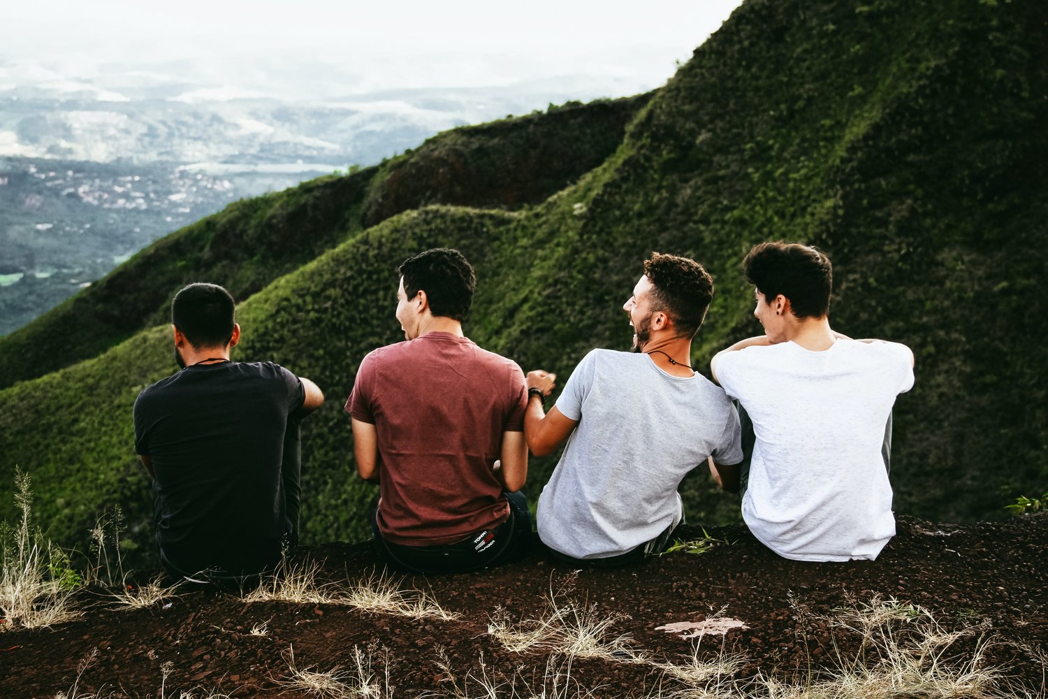 four males sitting on cliff overlooking mountains