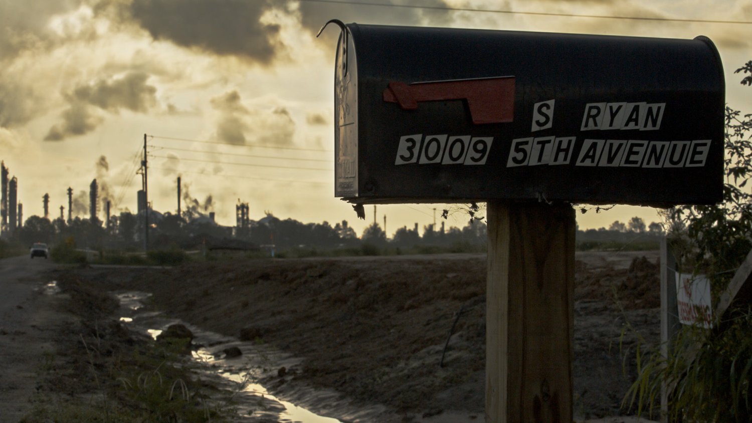 An image from the film 'Mossville- When Great Trees Fall' featuring a mailbox in an industrial landscape