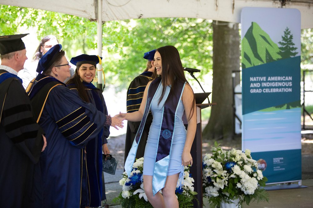 A student shaking the hands of their faculty at Native American and Indigenous Graduation
