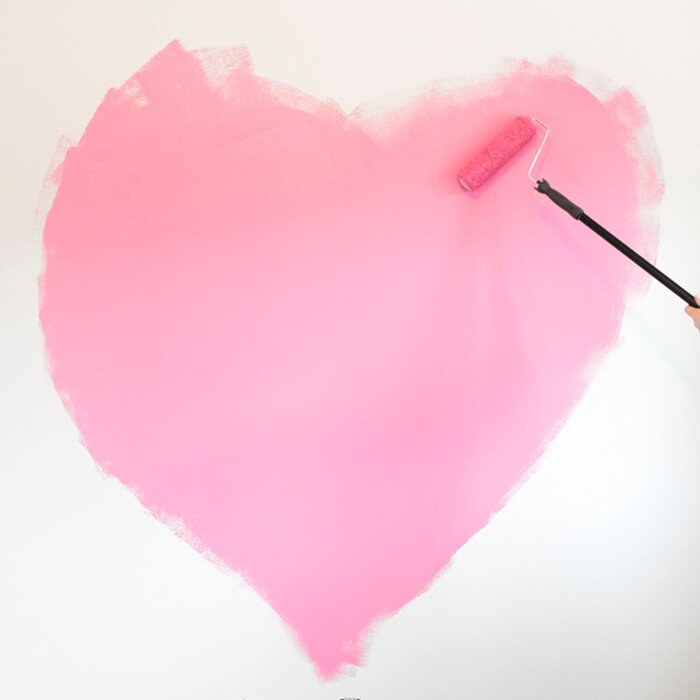 Someone painting a pink heart onto a white wall with a paint roller 