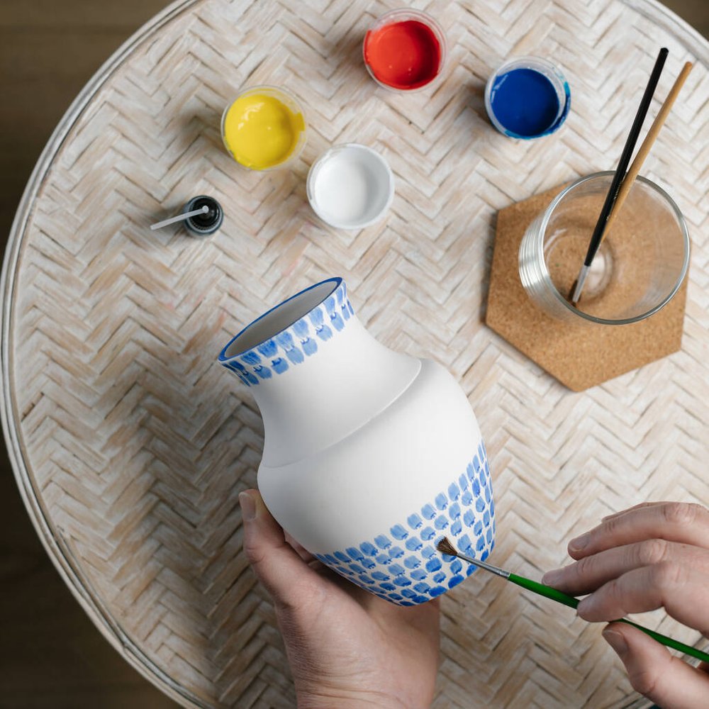 Someone painting blue dots on a ceramic piece of pottery