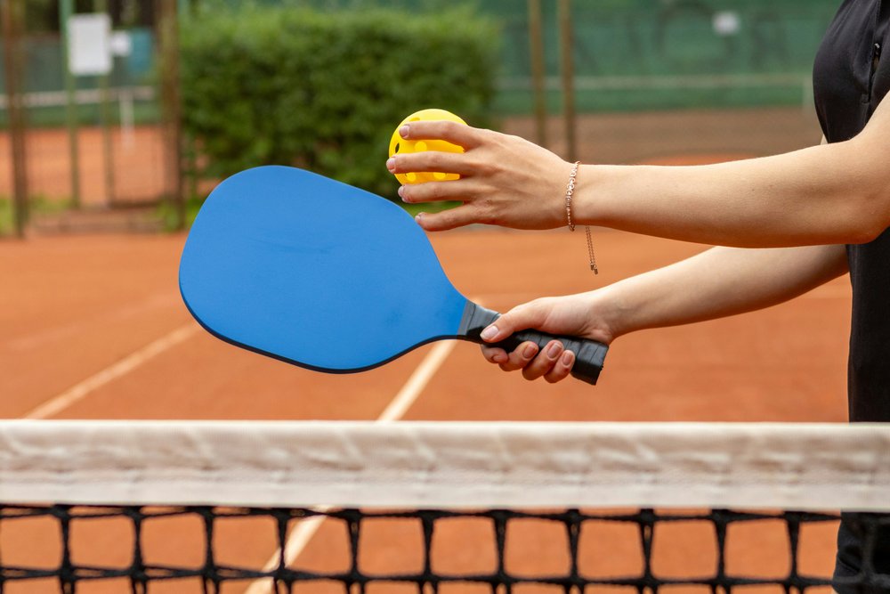 Someone serving a pickleball over a net 