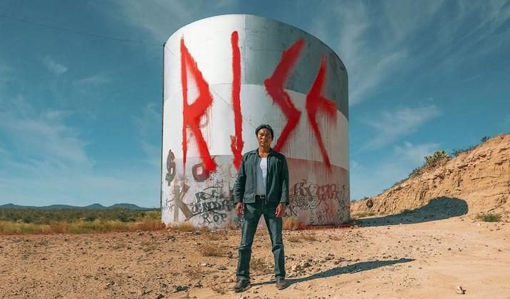 Image from the film 'Rise- Standing Rock' featuring someone standing in front of a water tank with the worse 'Rise' on it
