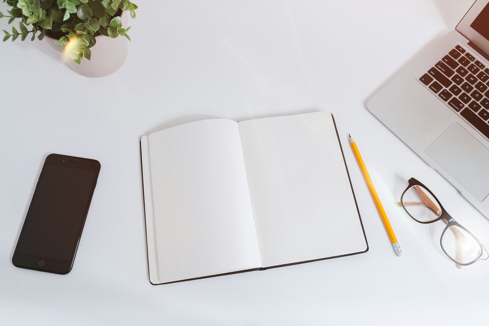 A notebook, pencil, phone, laptop, and eyeglasses