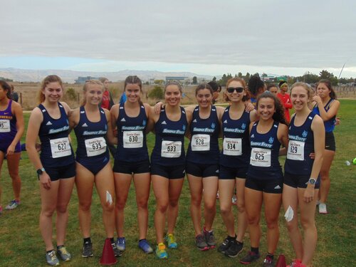 A line of eight cross country runners smiling while wearing running uniforms and numbers