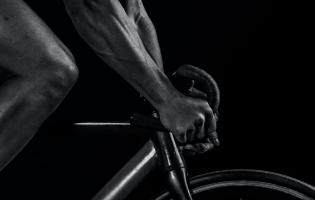 close up of hands on steering wheel on bicycle with knee in view in black and white