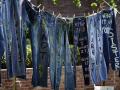 Multiple pairs of denim pants with writing on them hanging from a clothes line