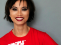 A portrait of Amazin LeThi smiling in a red t-shirt in front of a grey background