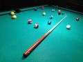 A pool cue and pool balls strewn across a billiard table