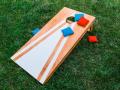 A wooden corn hole board with blue and red beanbags on top of green grass
