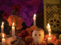 a sugar skull, multiple candles, and multiple orange marigold flowers for Día de los Muertos