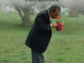 The film poster for 'I Am A Town' featuring a person in a suit smelling potted flowers while standing in a cemetery