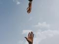 two hands reaching toward each other with the blue sky and white puffy clouds in the background