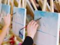 A row of people painting on canvases on easels 