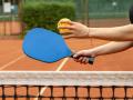 Someone serving a pickleball over a net 