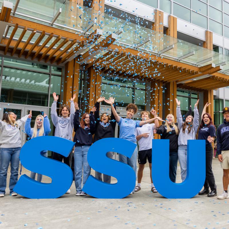 Students smiling and raising their hands celebrating outside the Student Center
