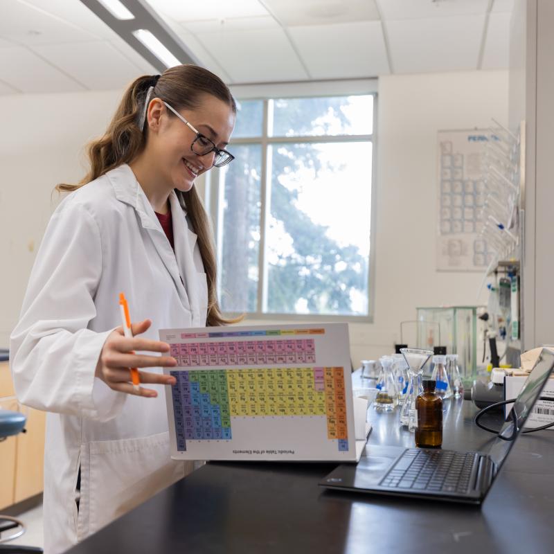 Studen in a lab with binder open with periodic table on the back