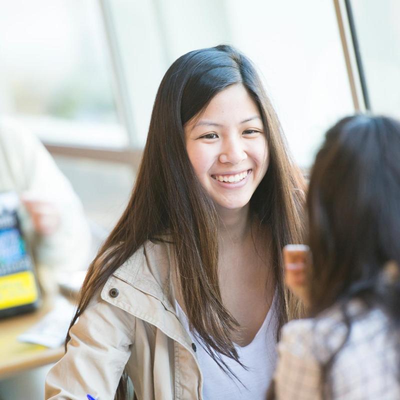 Person smiling and talking to another student while sitting at a table